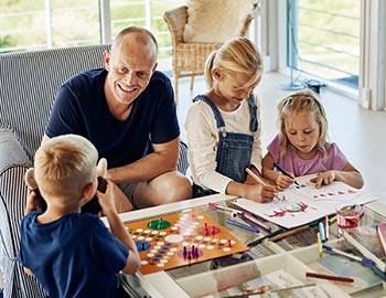 Vater und Kinder spielen ein Brettspiel und malen im Ferienhaus
